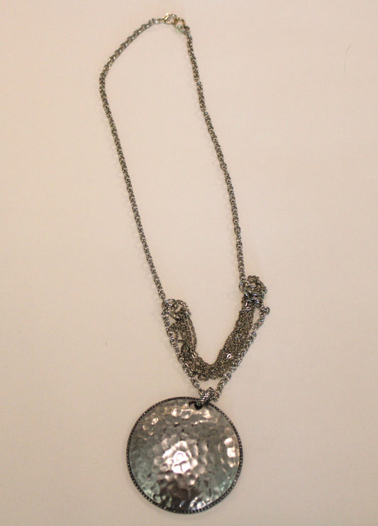 A silver necklace with a hammered disc on it.