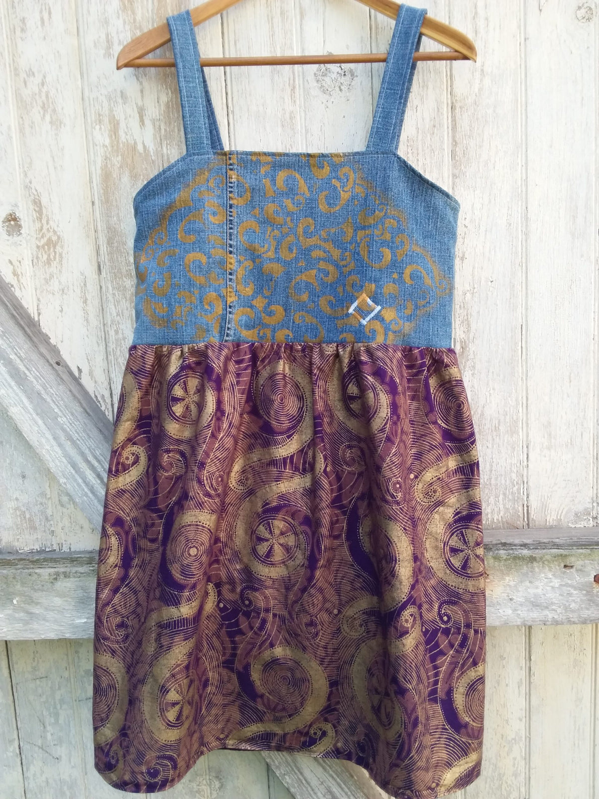 a gold and purple dress hanging on a wooden hanger.