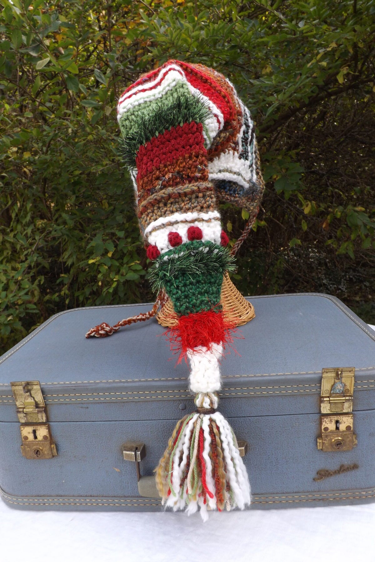 A crocheted elf hat sits on top of a suitcase.