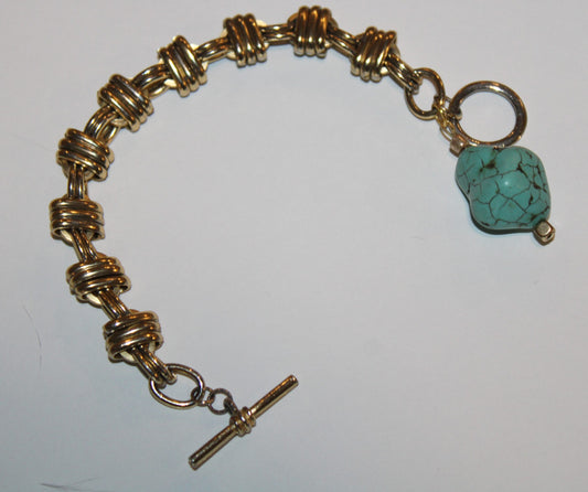 A gold bracelet with a turquoise stone.