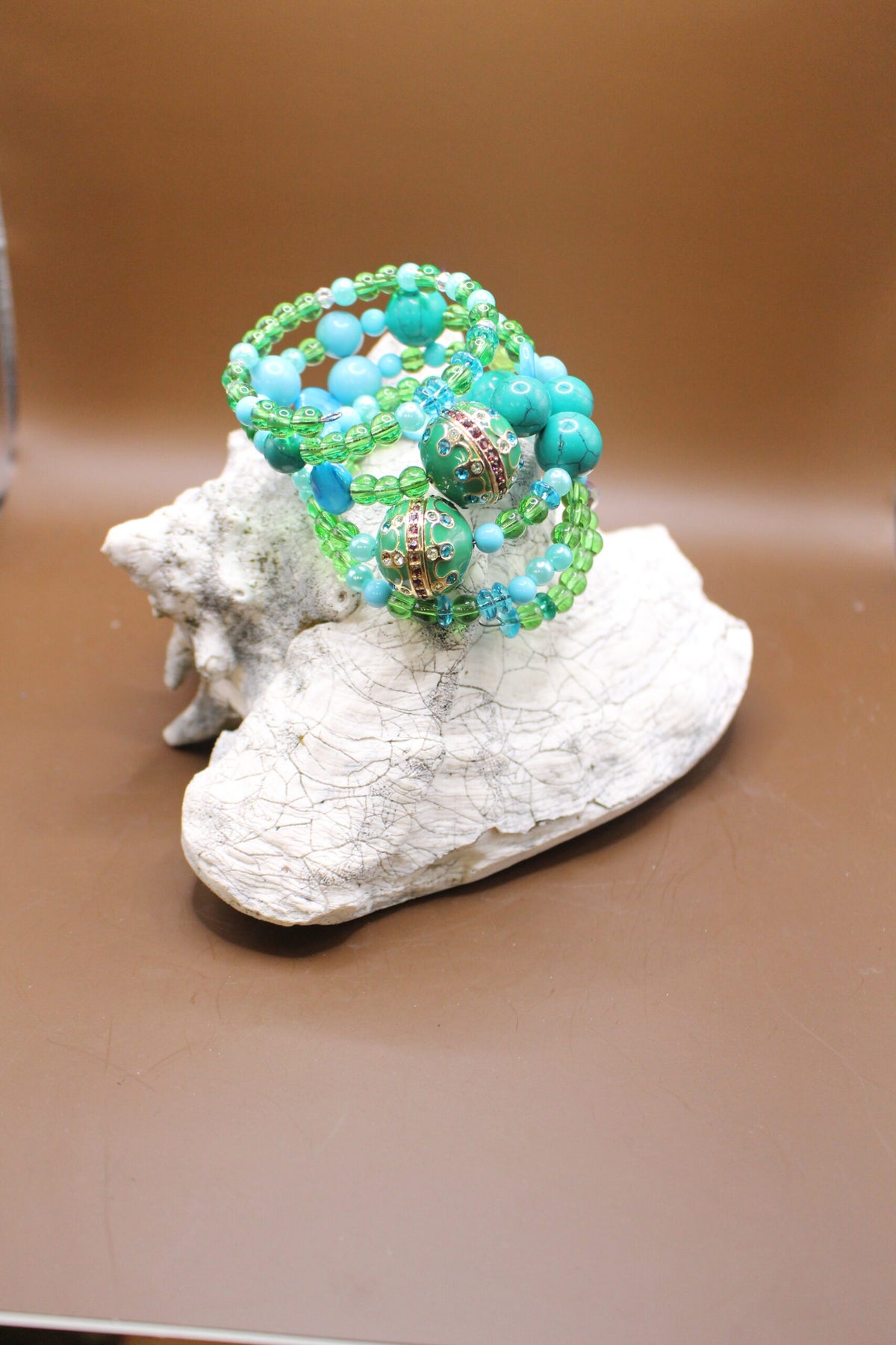 A beaded bracelet with green and blue beads on a white textured rock against a brown background.