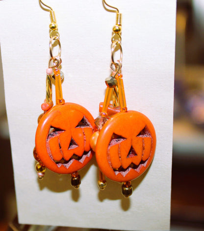 A pair of orange jack o lantern earrings hanging on a piece of paper.