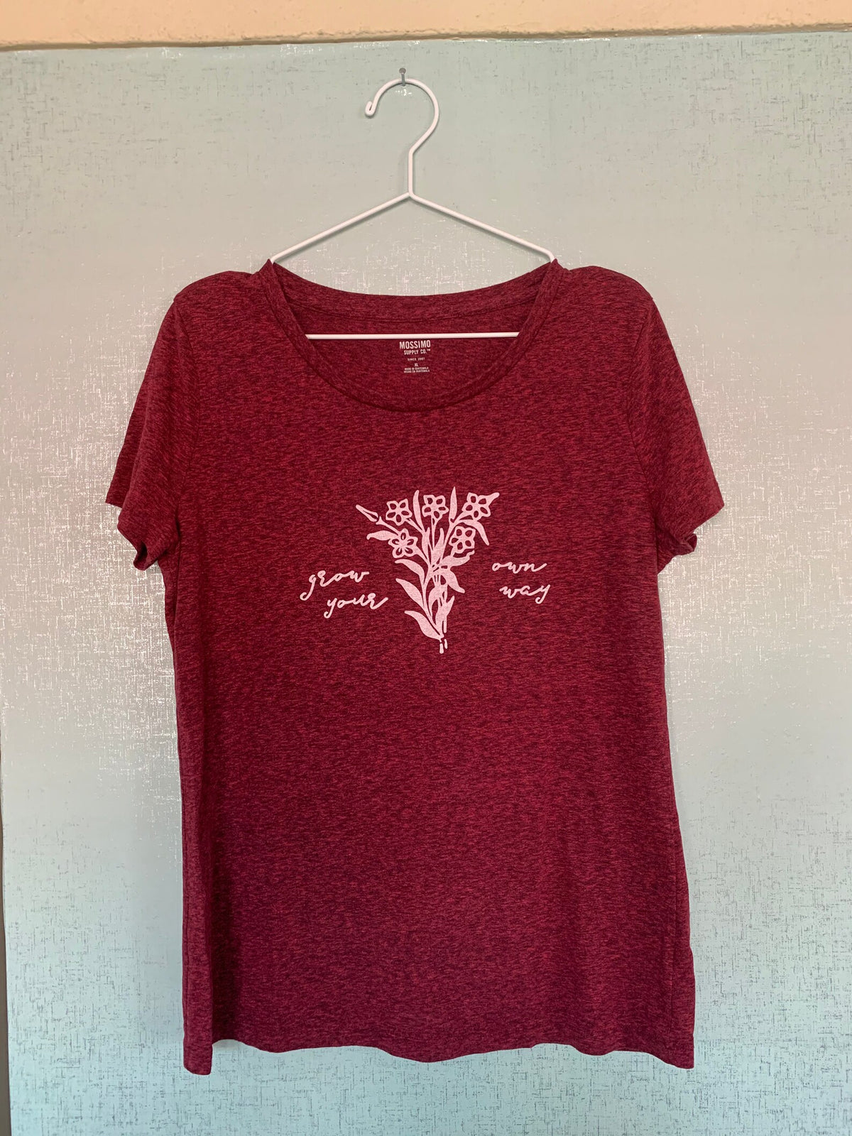 A women's red t - shirt hanging on a wall.