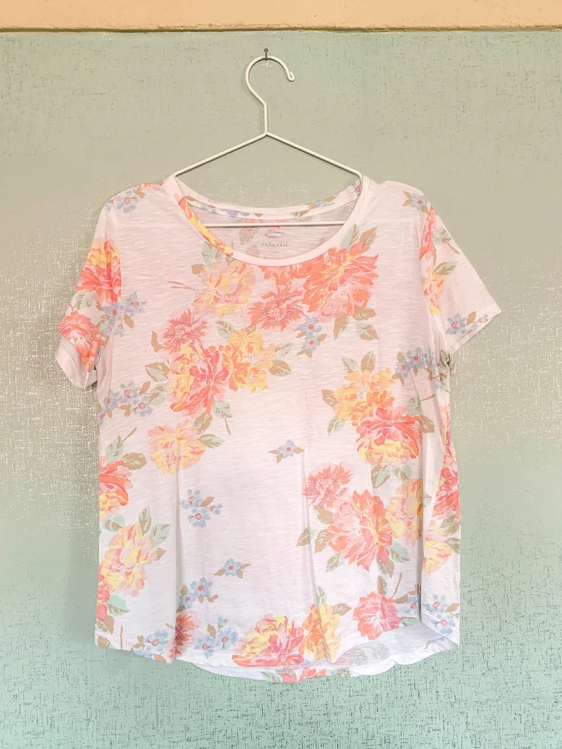 A white and pink floral t - shirt hanging on a hanger.