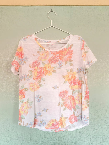 A white and pink floral t - shirt hanging on a hanger.