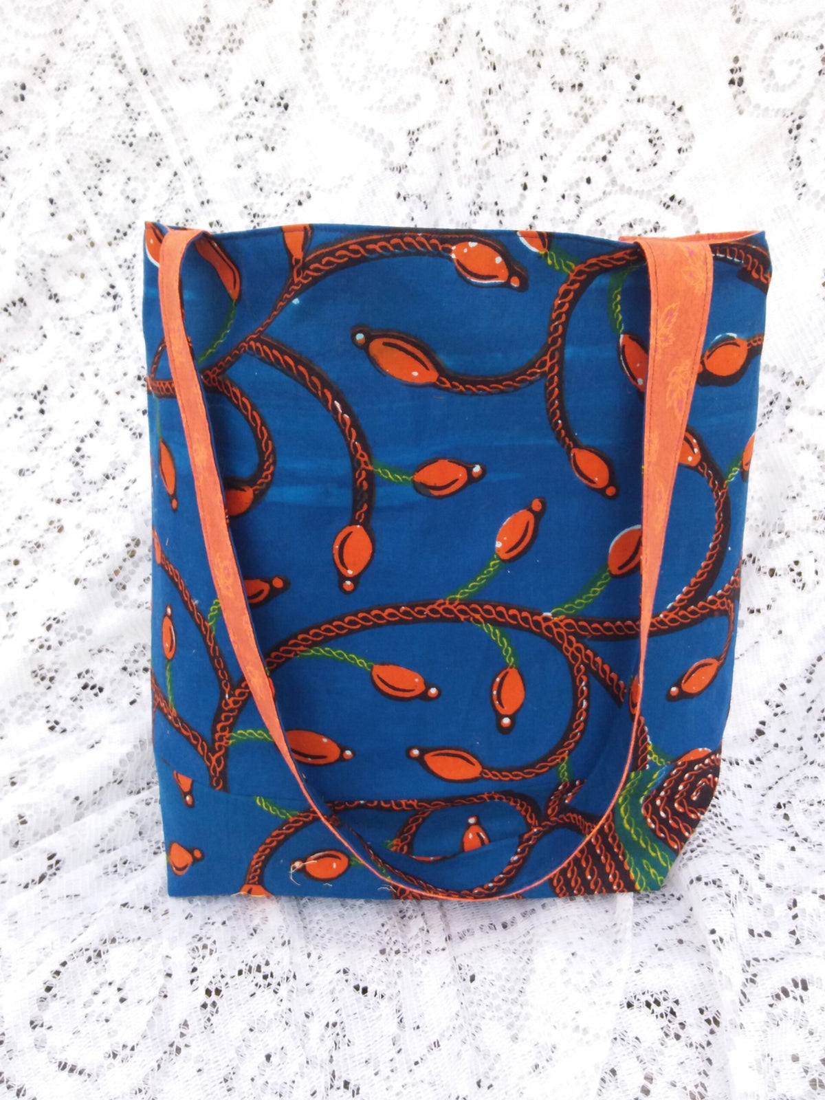A large market tote handcrafted from vintage blue and orange Tree of Life fabric sits upon a lace background