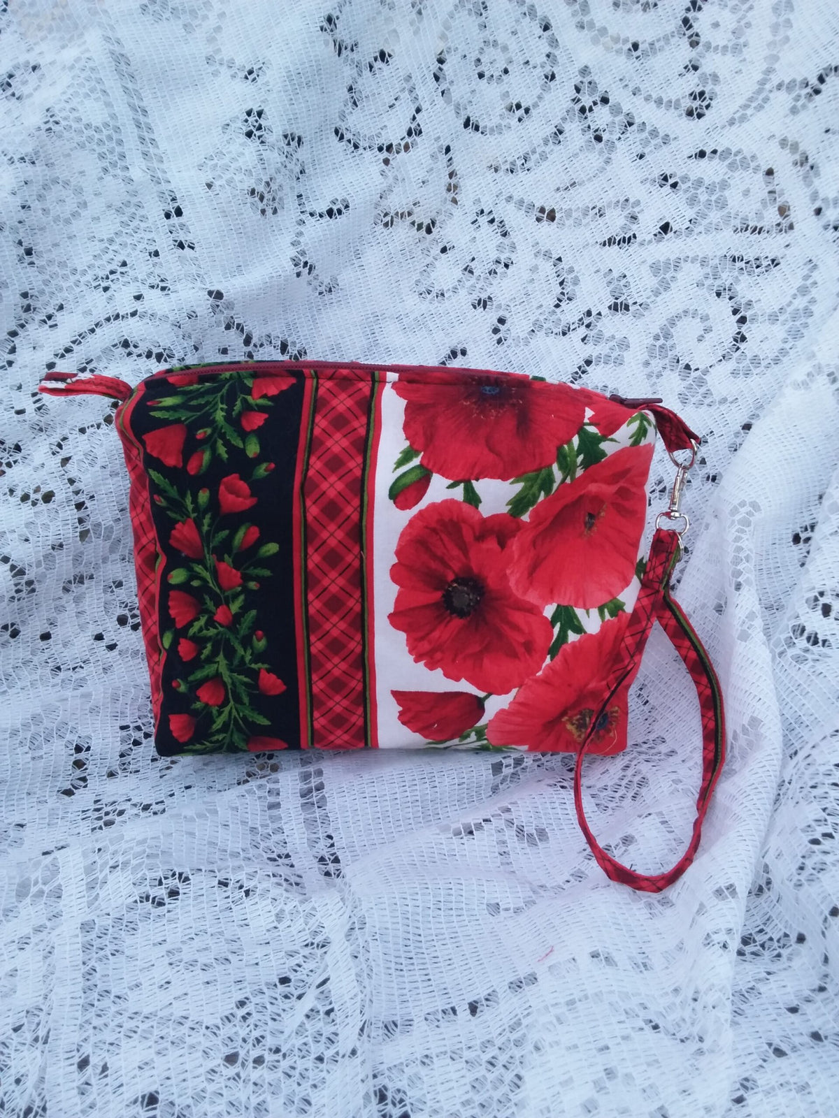 Bold poppy fabric, handcrafted into a quilted wristlet bag rests upon a vintage lace background.