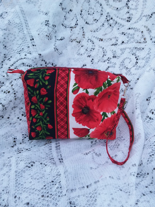 Bold poppy fabric, handcrafted into a quilted wristlet bag rests upon a vintage lace background.