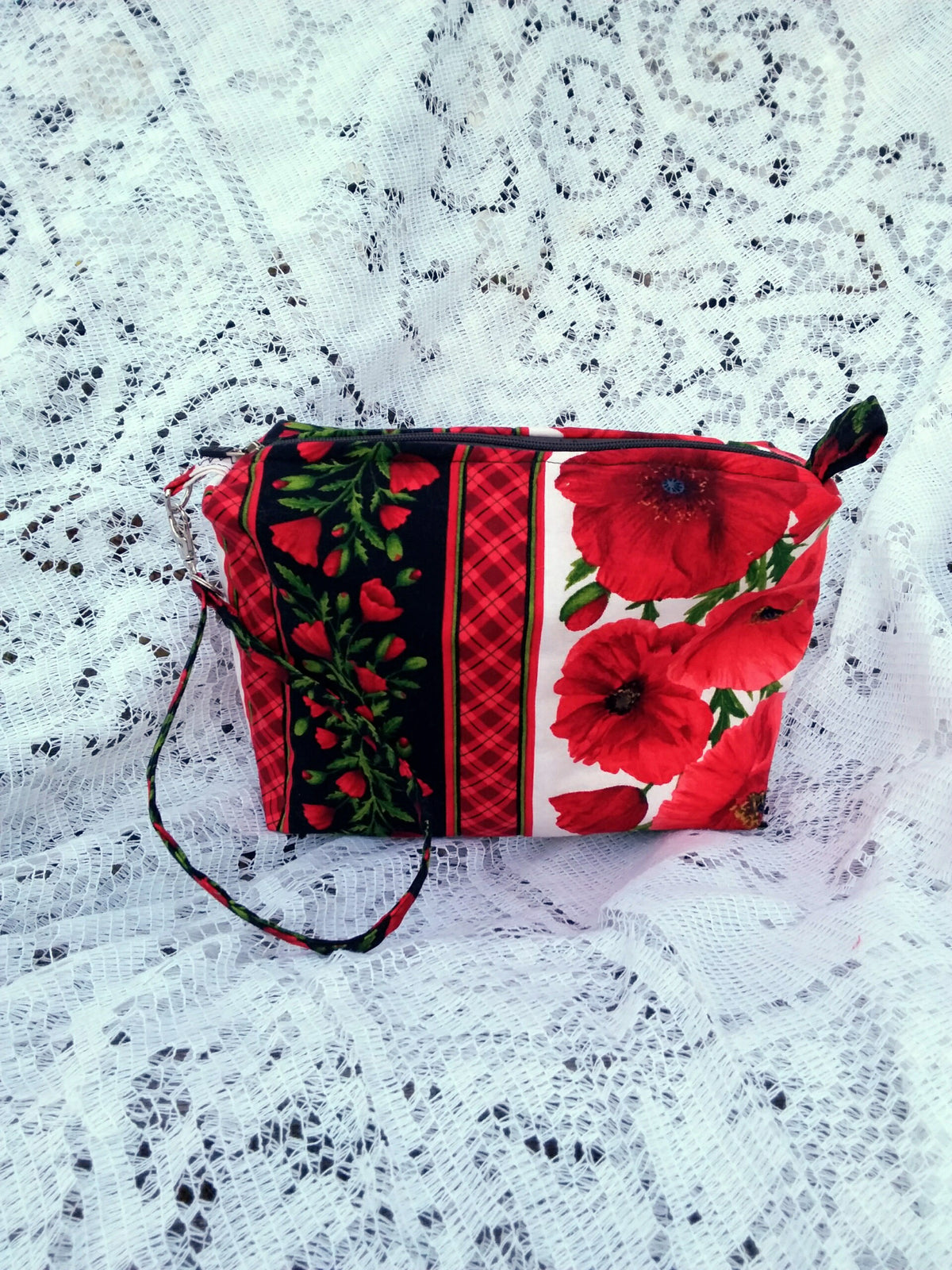 Bold poppy fabric, handcrafted into a quilted wristlet bag rests upon a vintage lace background.