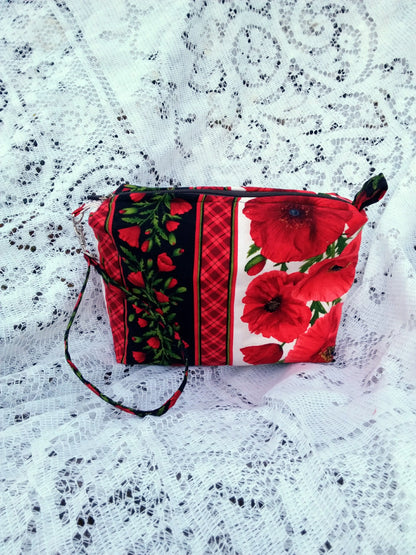 Bold poppy fabric, handcrafted into a quilted wristlet bag rests upon a vintage lace background.