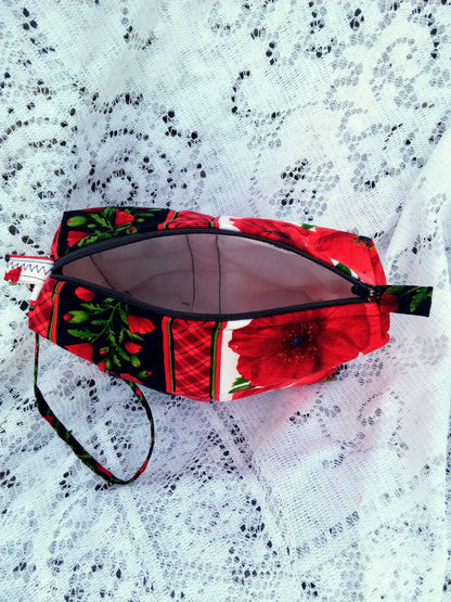 Bold poppy fabric, handcrafted into a quilted wristlet bag rests upon a vintage lace background.