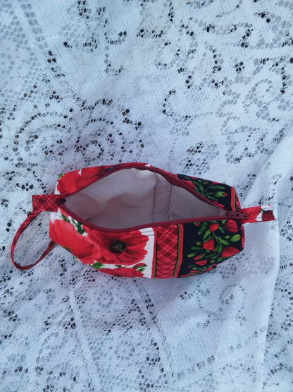 Bold poppy fabric, handcrafted into a quilted wristlet bag rests upon a vintage lace background.