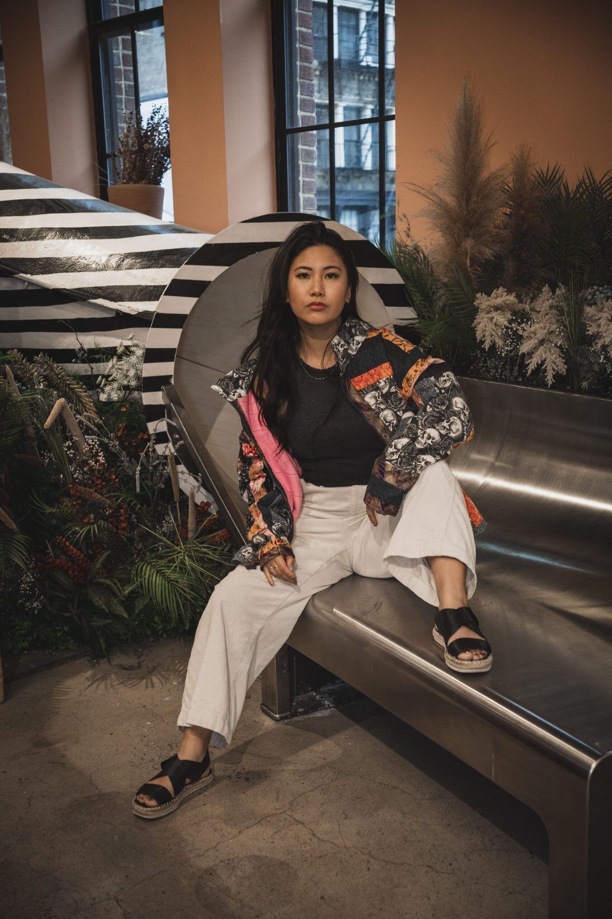 A woman sitting on a metal bench in front of plants.