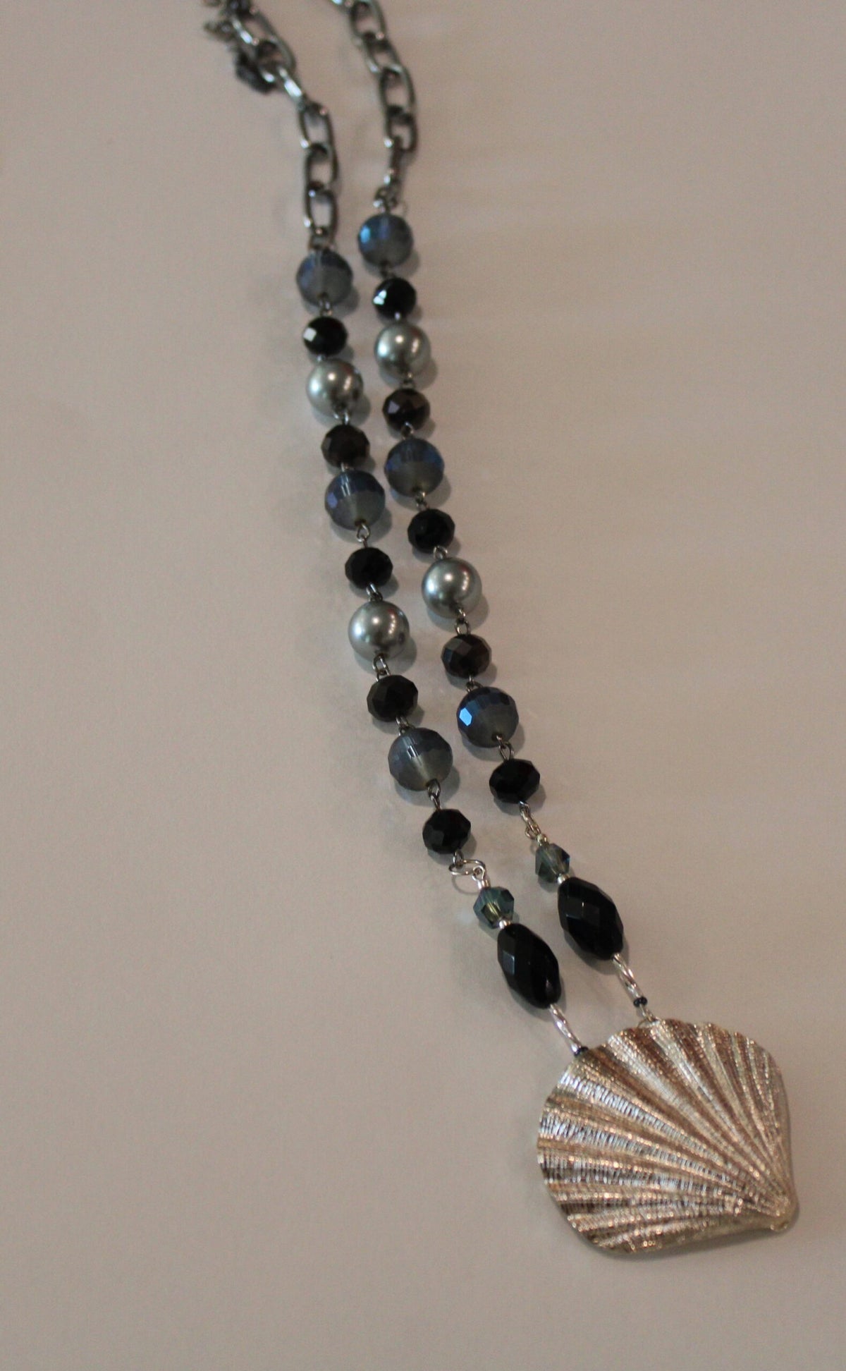 A necklace with a silver shell and black beads.