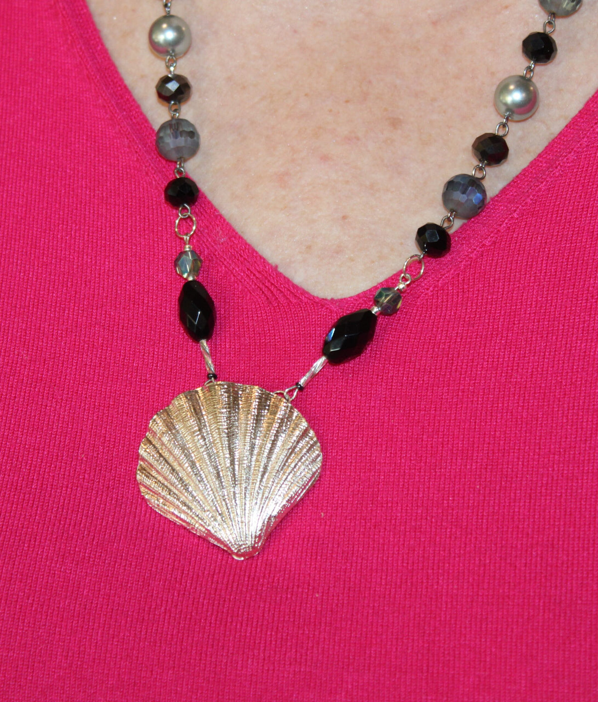 A woman is wearing a necklace with a shell on it.