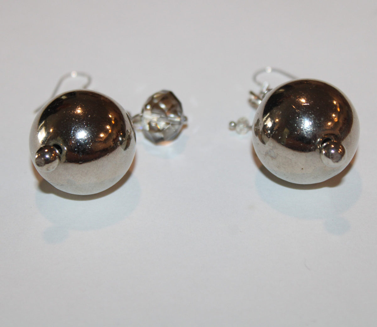 A pair of silver ball earrings on a white surface.