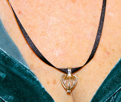 pearl encased in silver heart cage with black ribbon cord on a model
