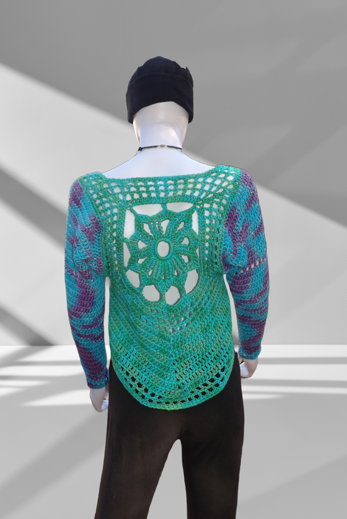 A crochet sweater with sun design in shades of green, blue and purple.