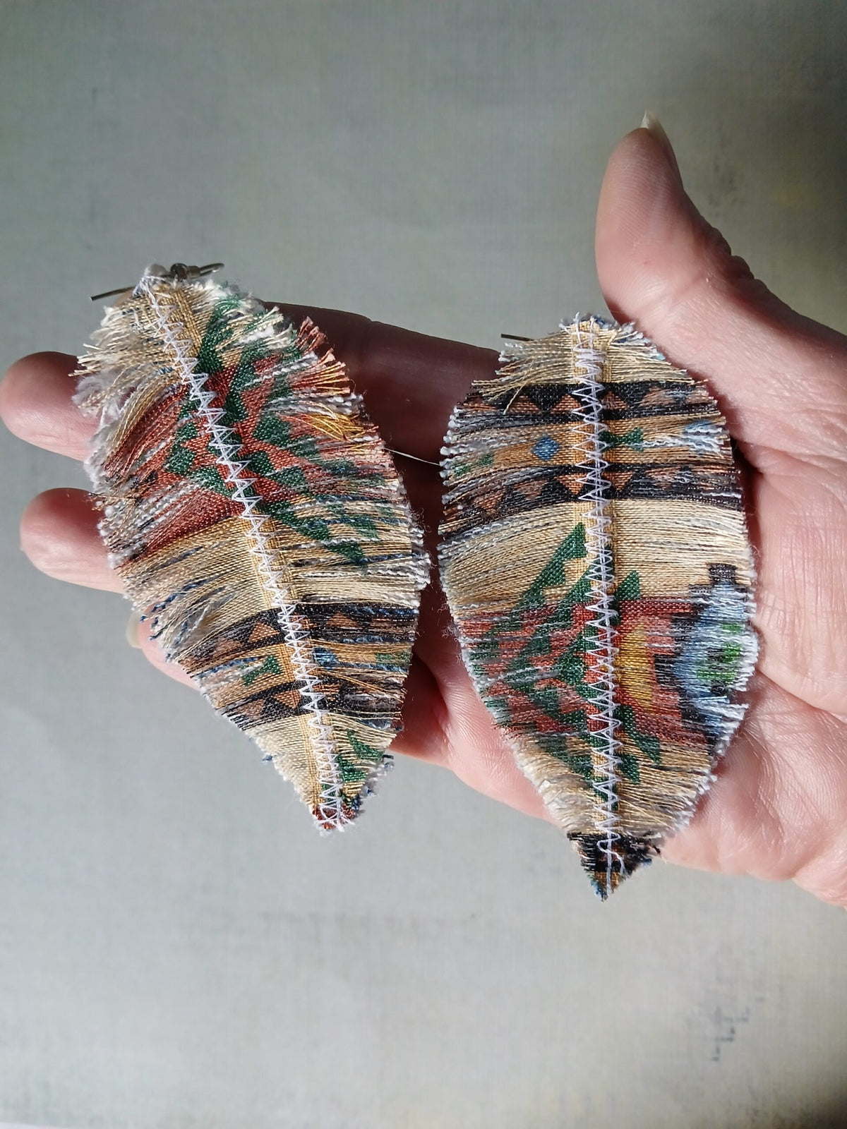 A person holding a pair of leaf earrings.