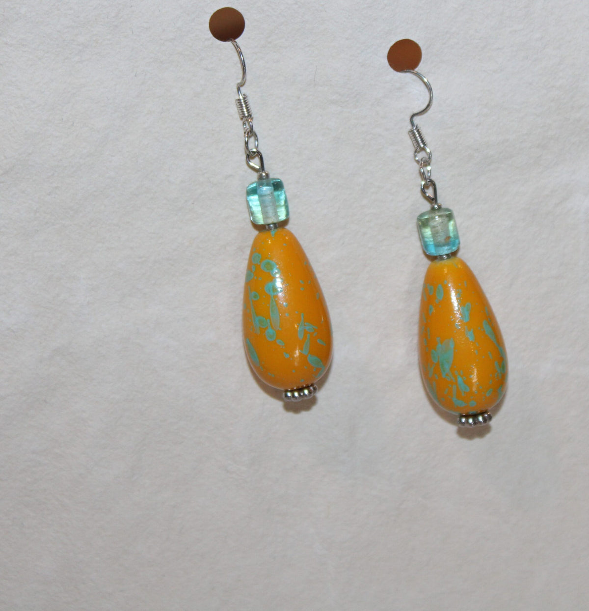 A pair of yellow and turquoise earrings hanging on a white surface.