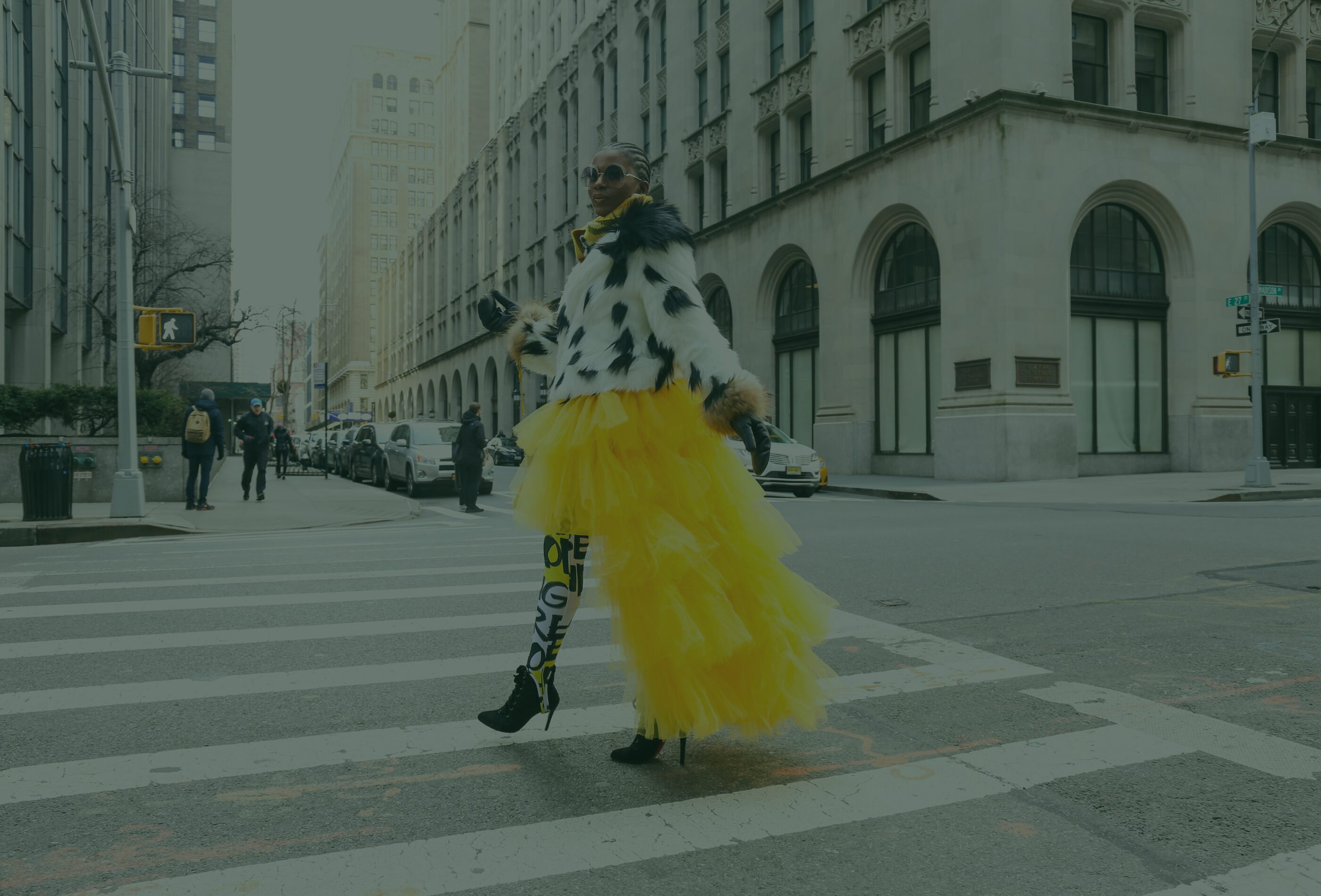 a woman is crossing the street in a yellow dress.