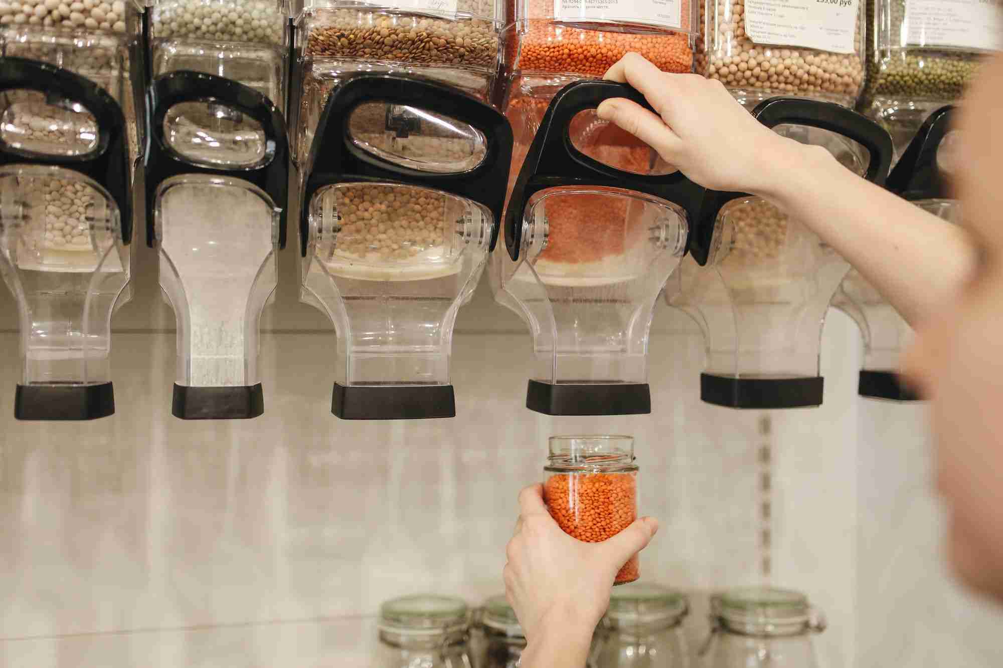 a person holding a jar of food in front of a spice rack.
