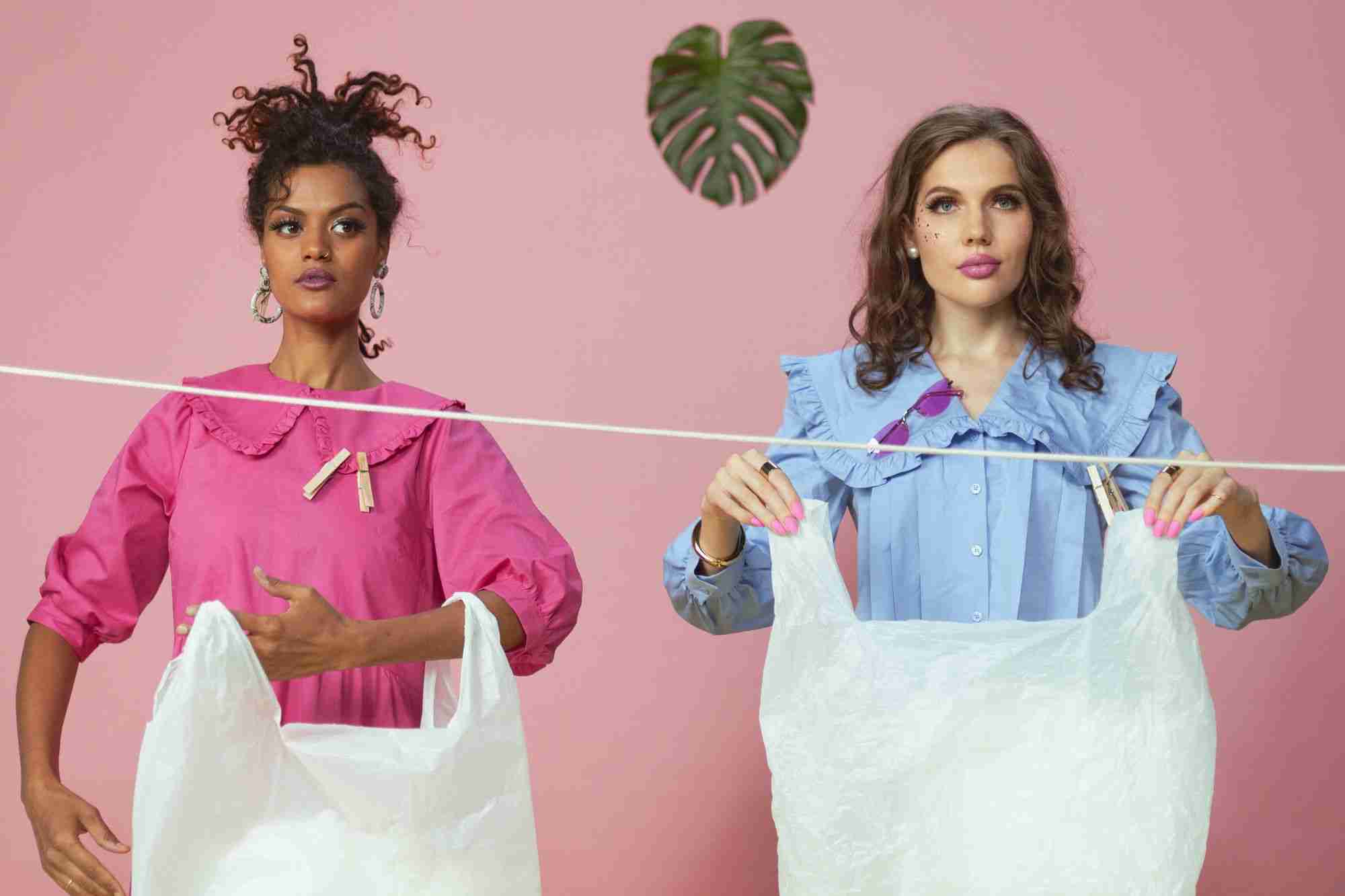 two women holding shopping bags in front of a pink wall.