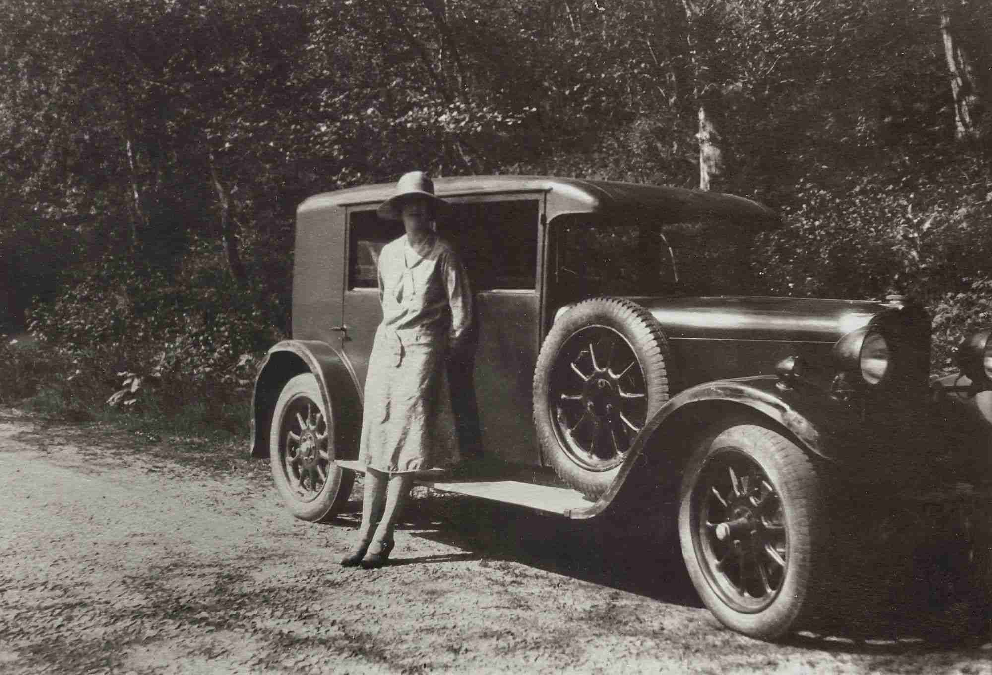 a woman standing next to an old car on a dirt road.