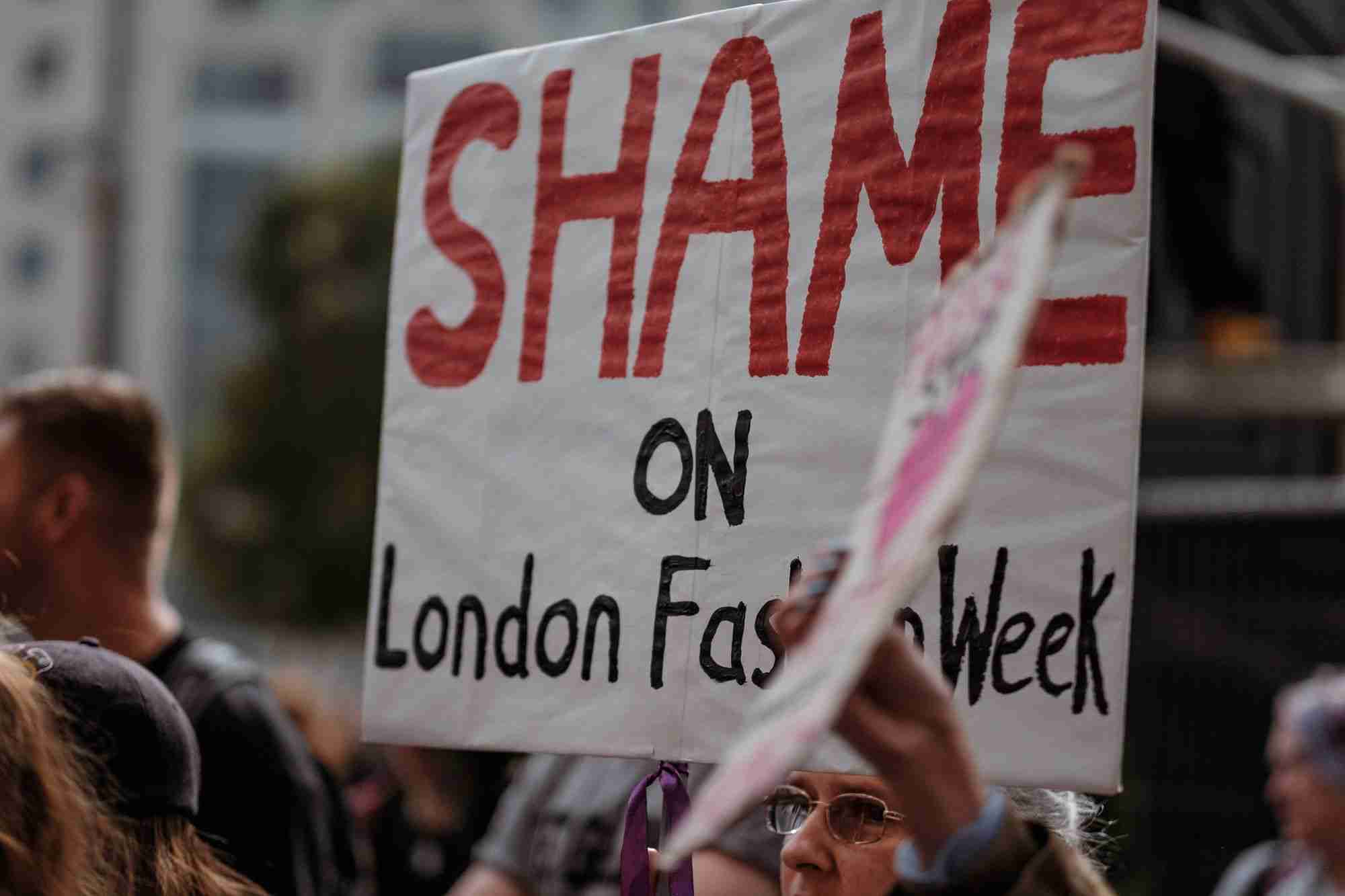 a woman holding a sign that says shame on london fast week.