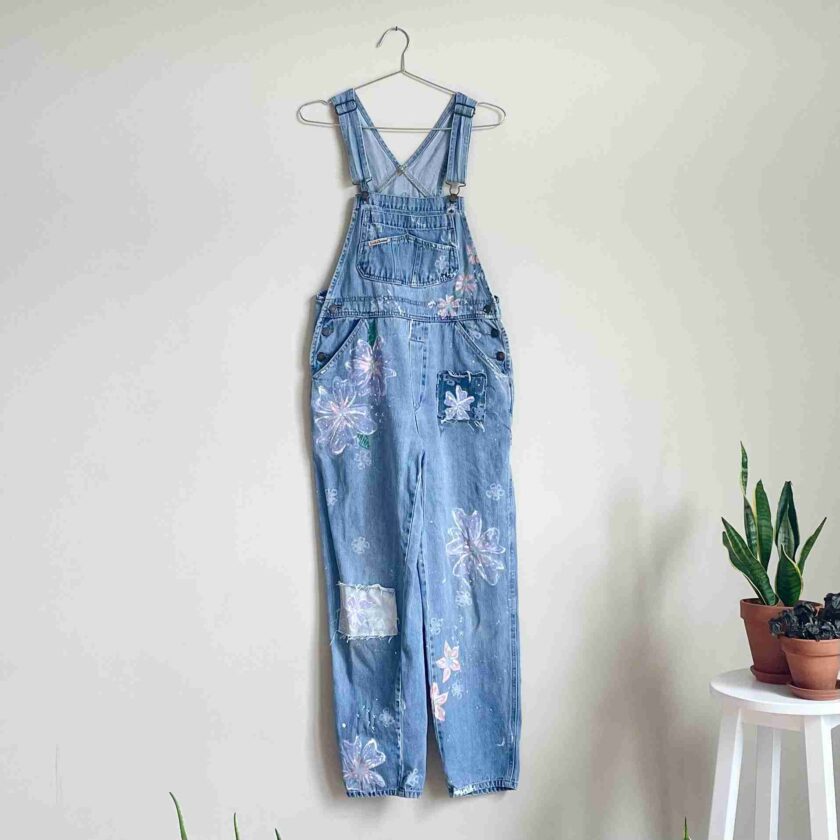 a blue jean jumpsuit hanging on a wall next to a potted plant.