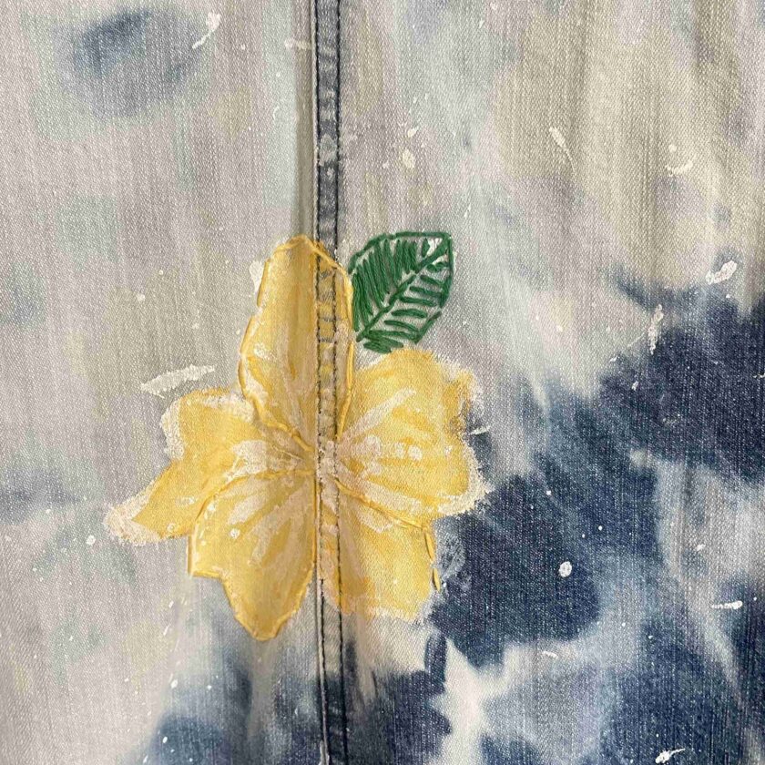 a close up of a yellow flower on a tie dye shirt.