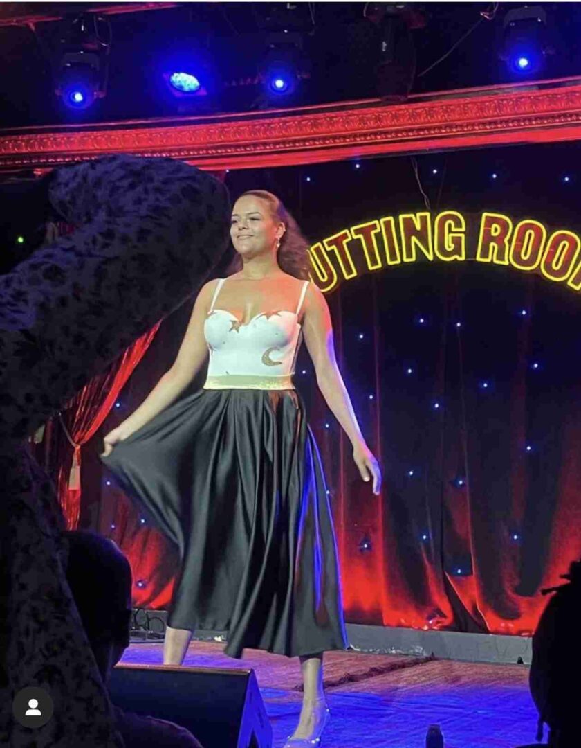 a woman in a white top and black skirt on a stage.