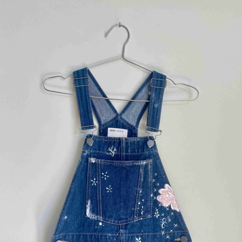 a pair of denim overalls hanging on a hanger.