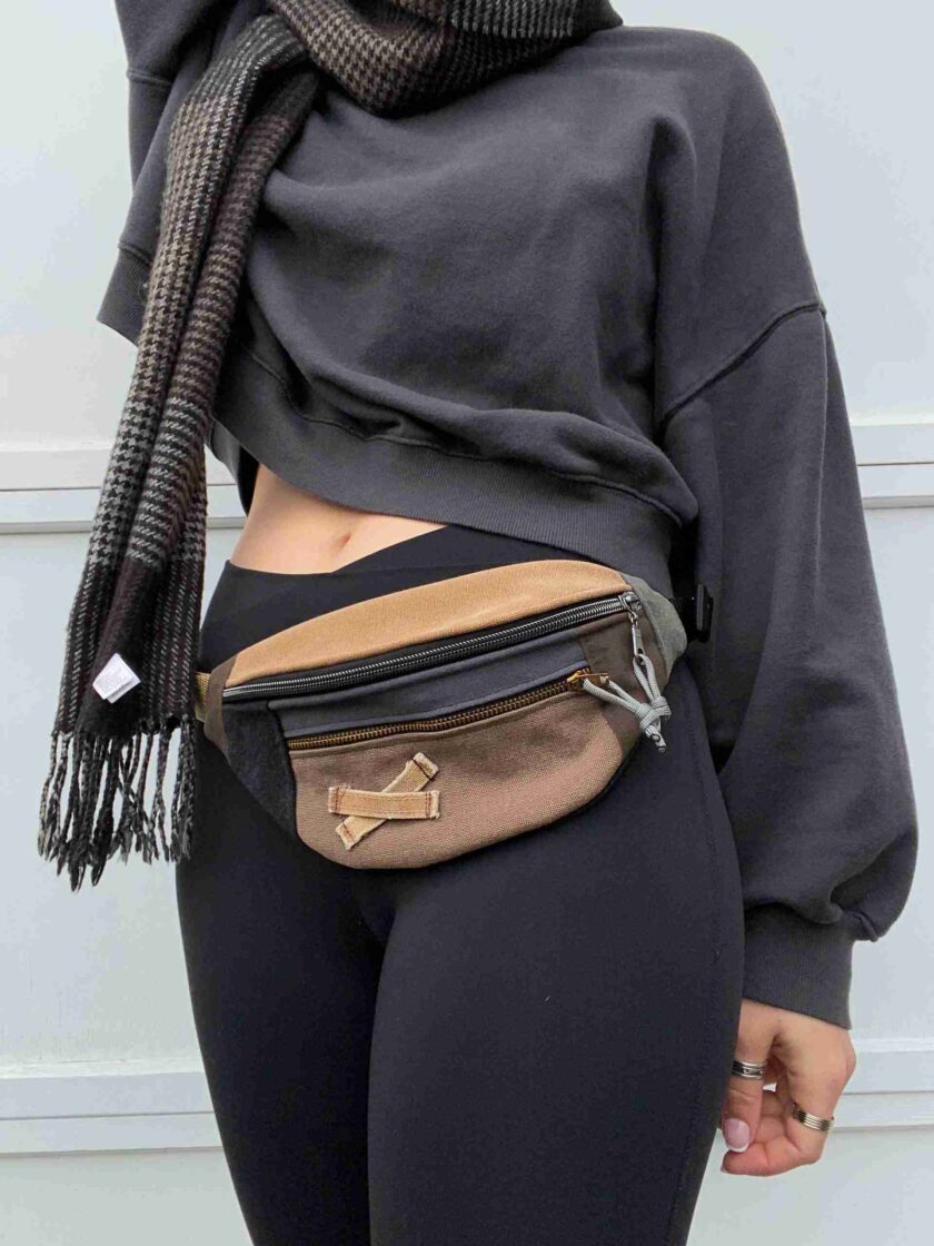 a woman wearing a black hoodie and a tan fanny bag.