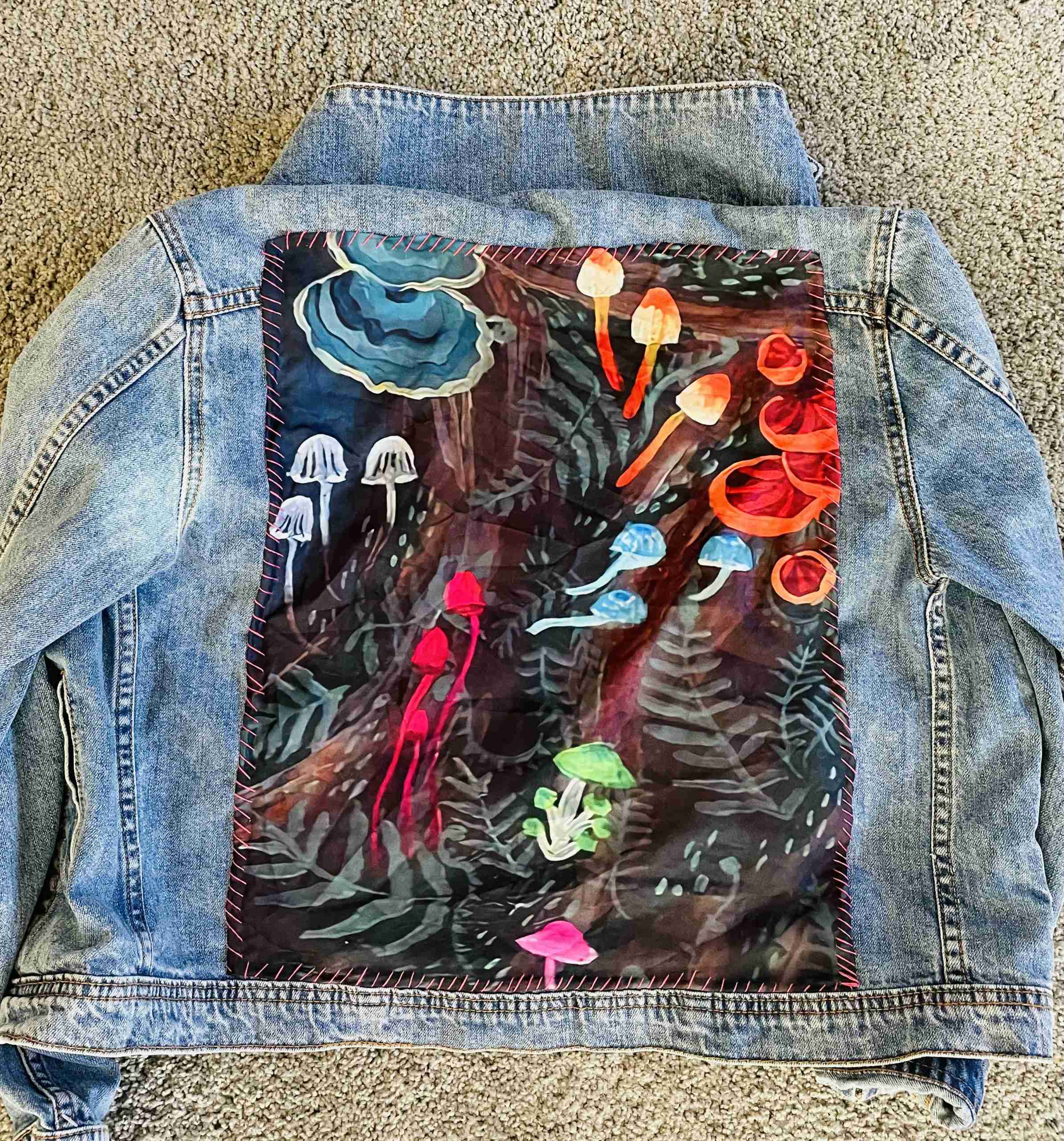 a jean jacket with a painting on the back of it.