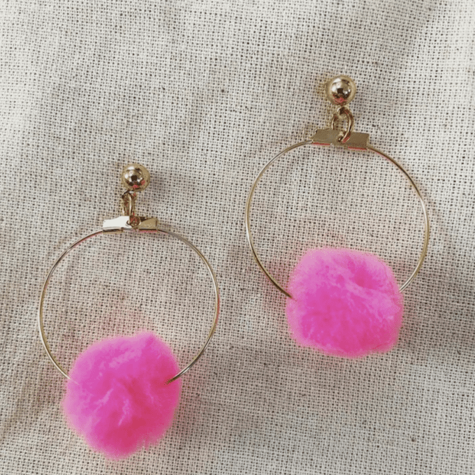 a pair of hoop earrings with pink pom pom.