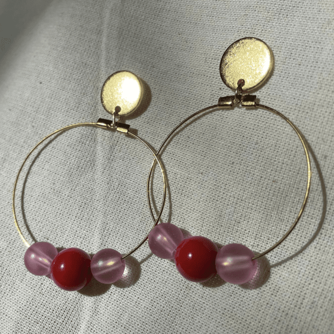 a pair of gold hoop earrings with pink and red beads.