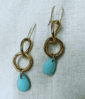 a pair of gold and turquoise earrings on a white cloth.