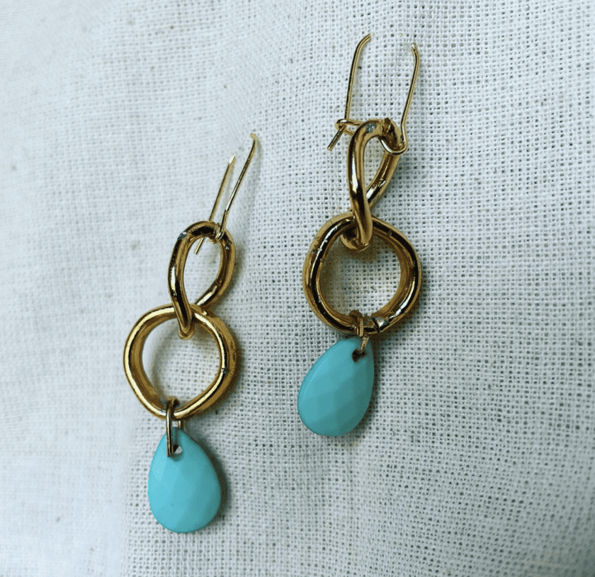 a pair of gold and turquoise earrings on a white cloth.