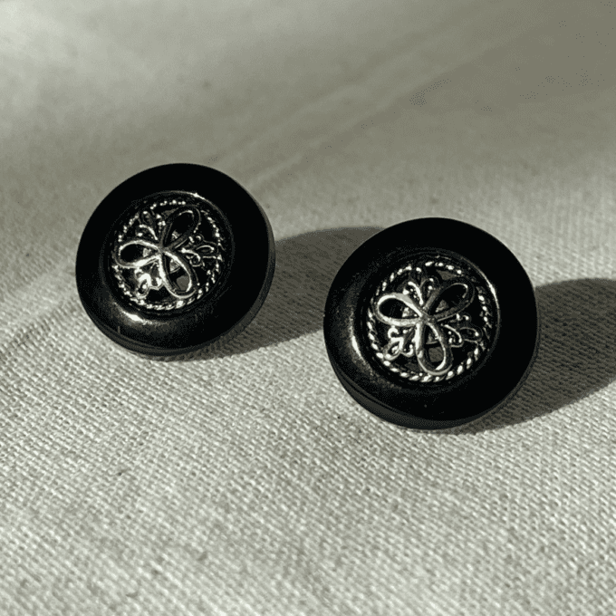 a pair of black and silver earrings sitting on top of a white cloth.