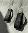 a pair of black leather earrings on a white cloth.