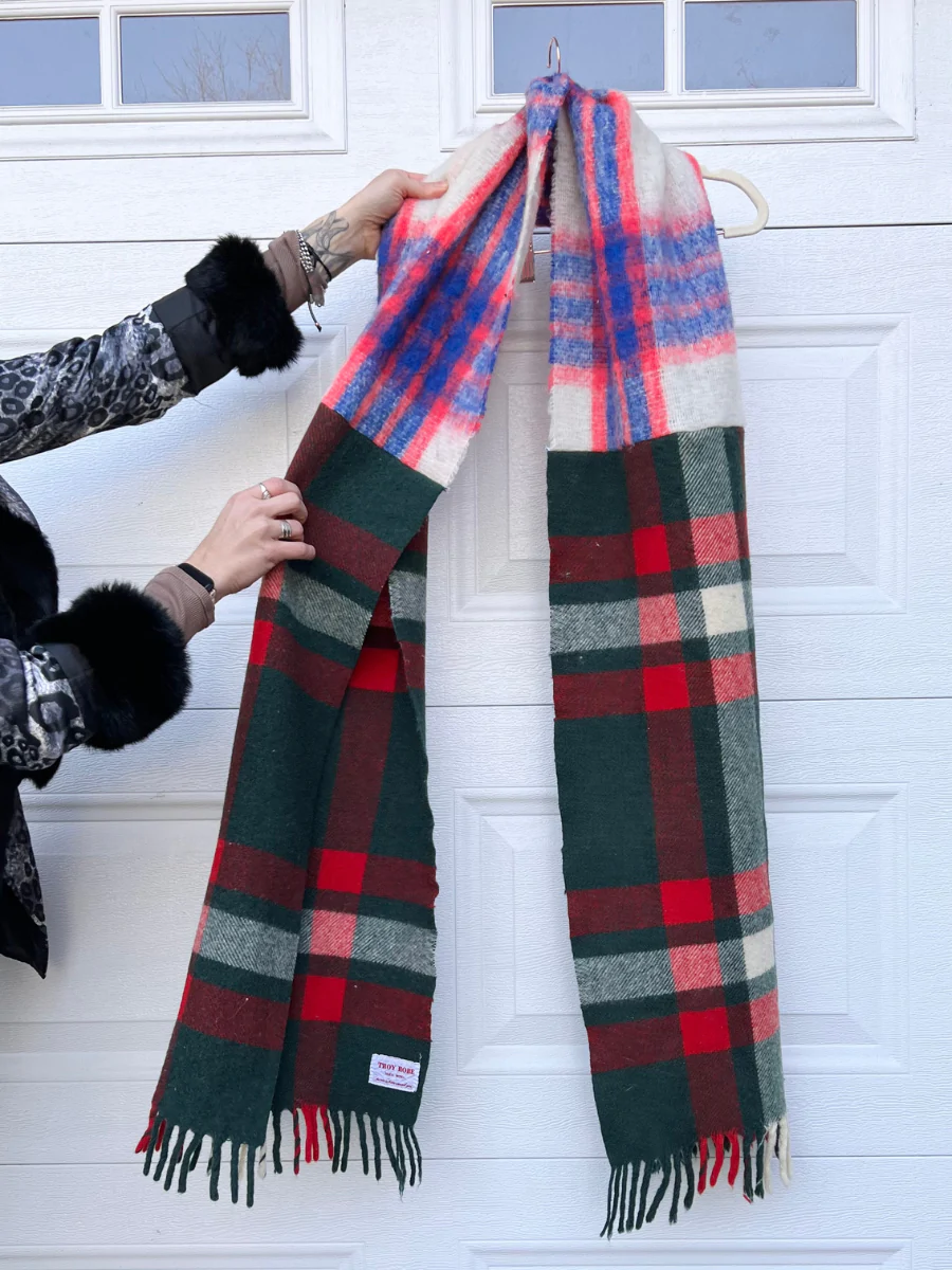 a woman is holding a plaid scarf in front of a garage door.