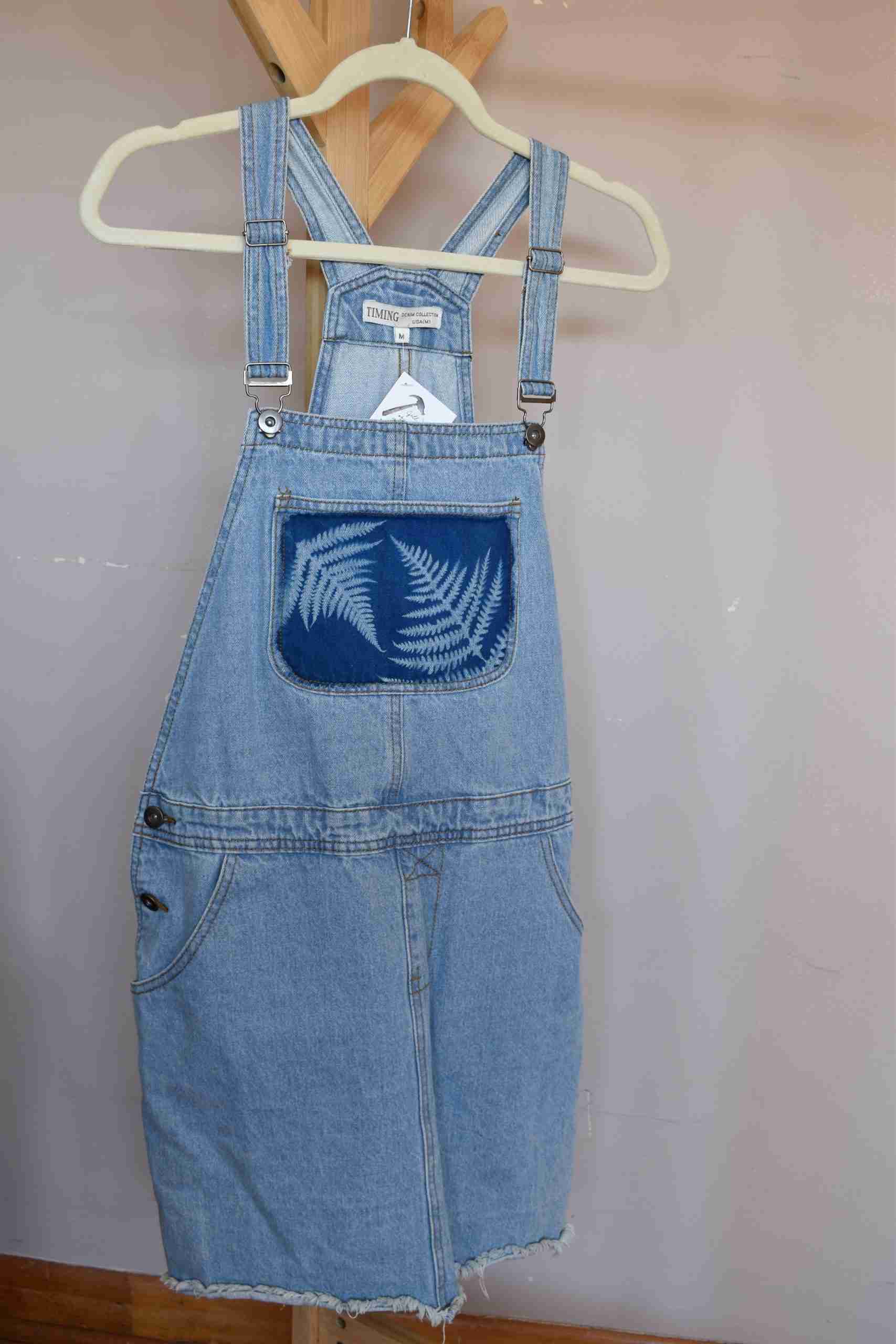 a pair of blue denim overalls hanging on a wooden hanger.
