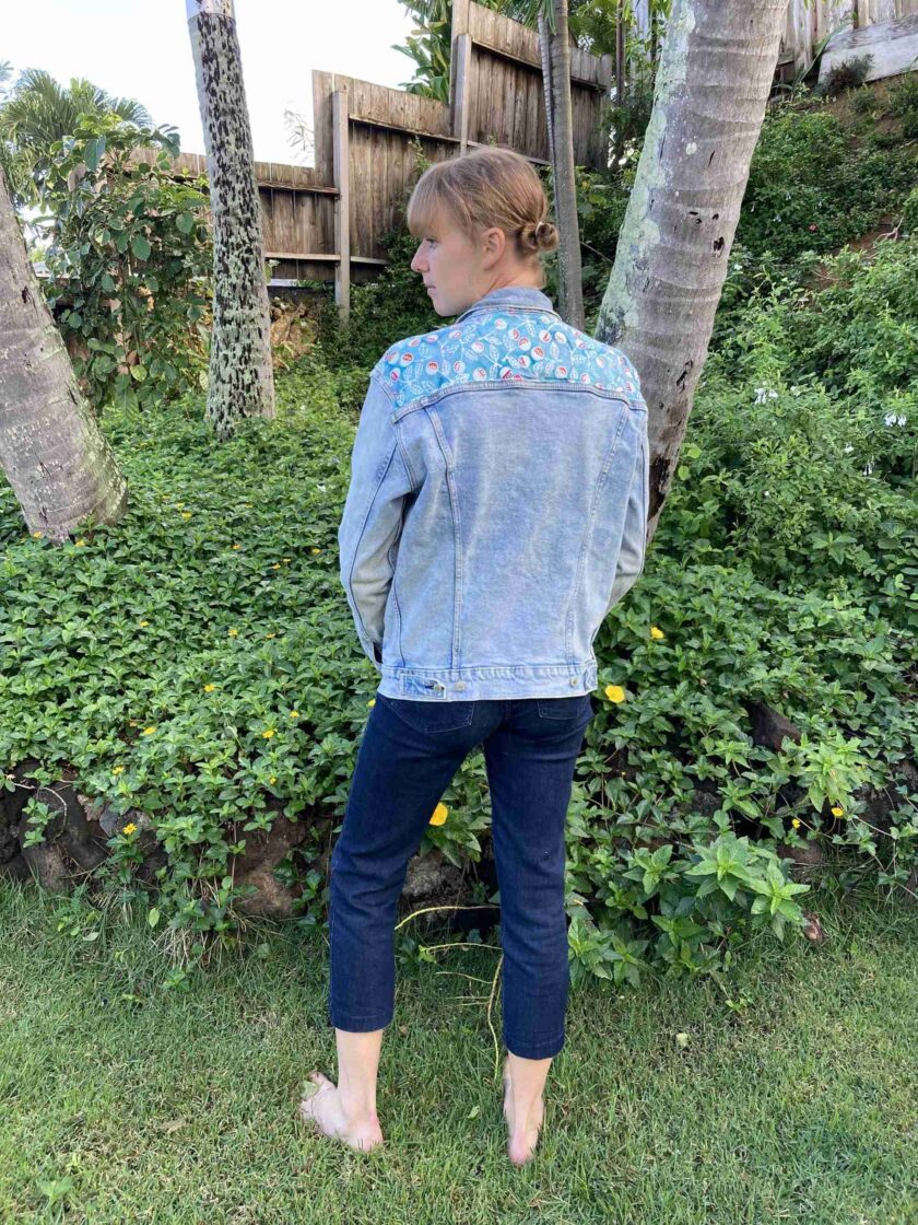 a woman standing in the grass wearing a jean jacket.