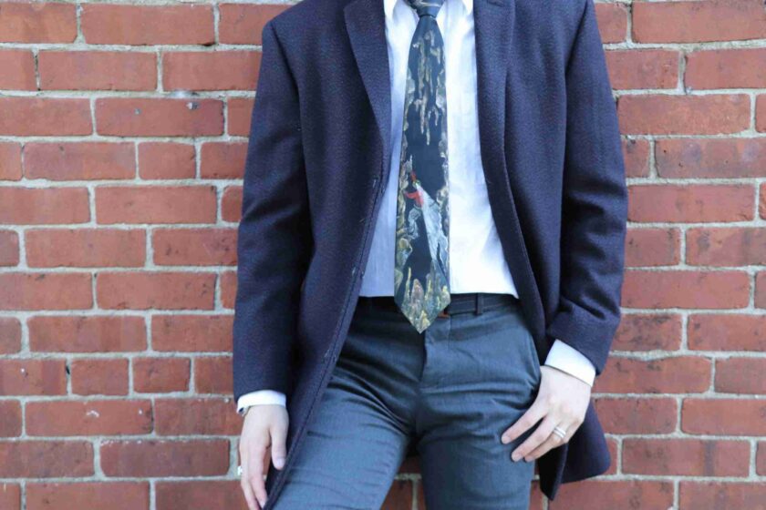 a man in a suit and tie leaning against a brick wall.