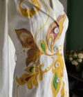 a white dress with yellow and green designs on it.