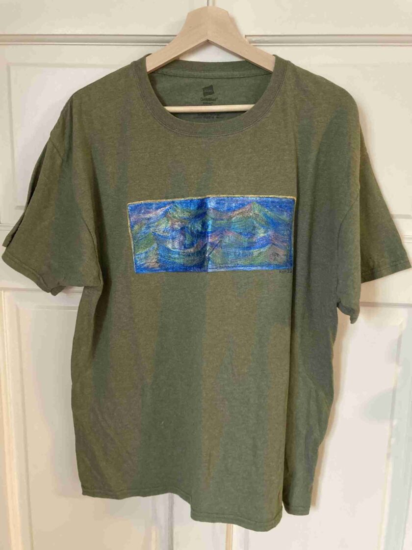 a t - shirt hanging on a door with a painting on it.