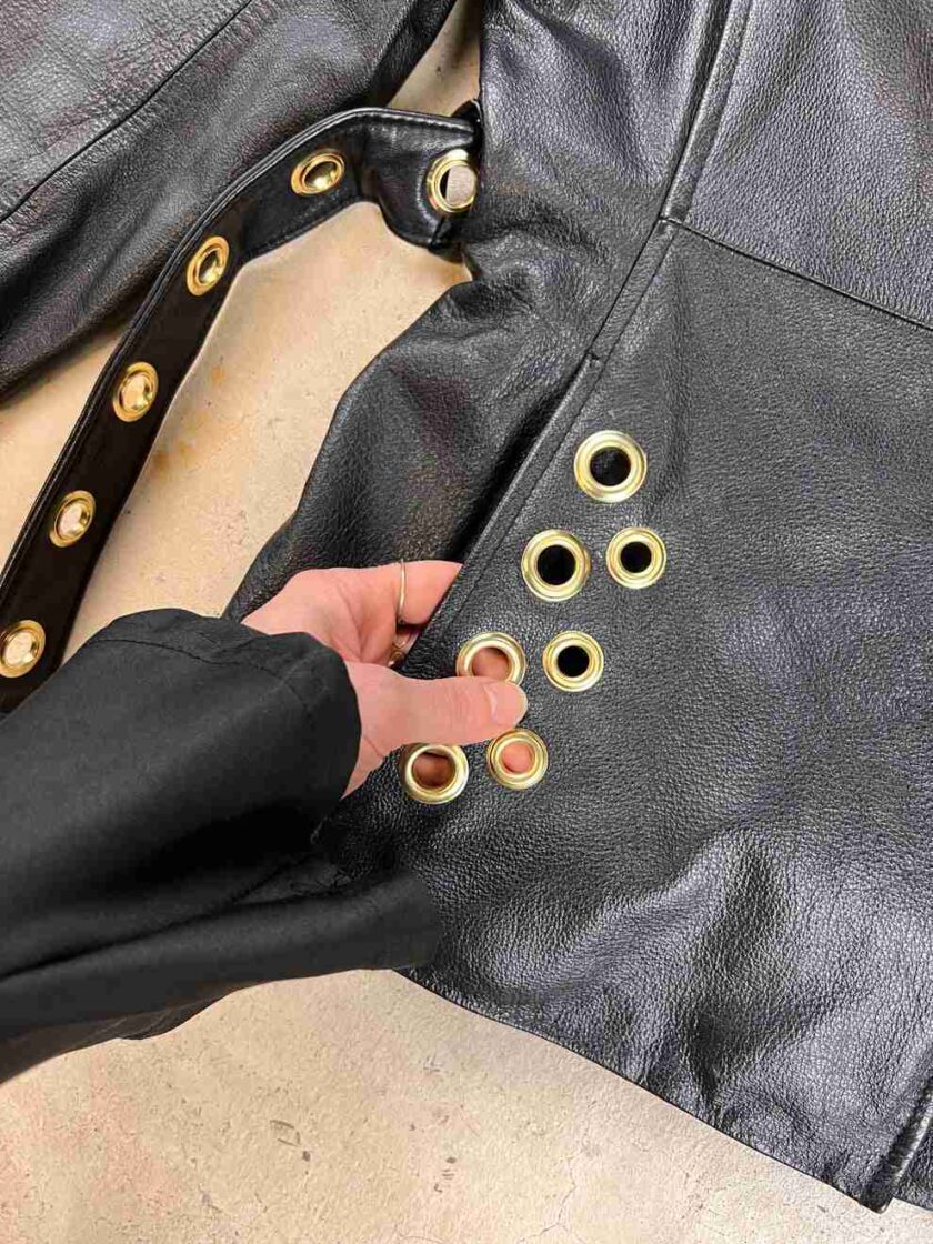 a person holding a black leather jacket with gold buttons.