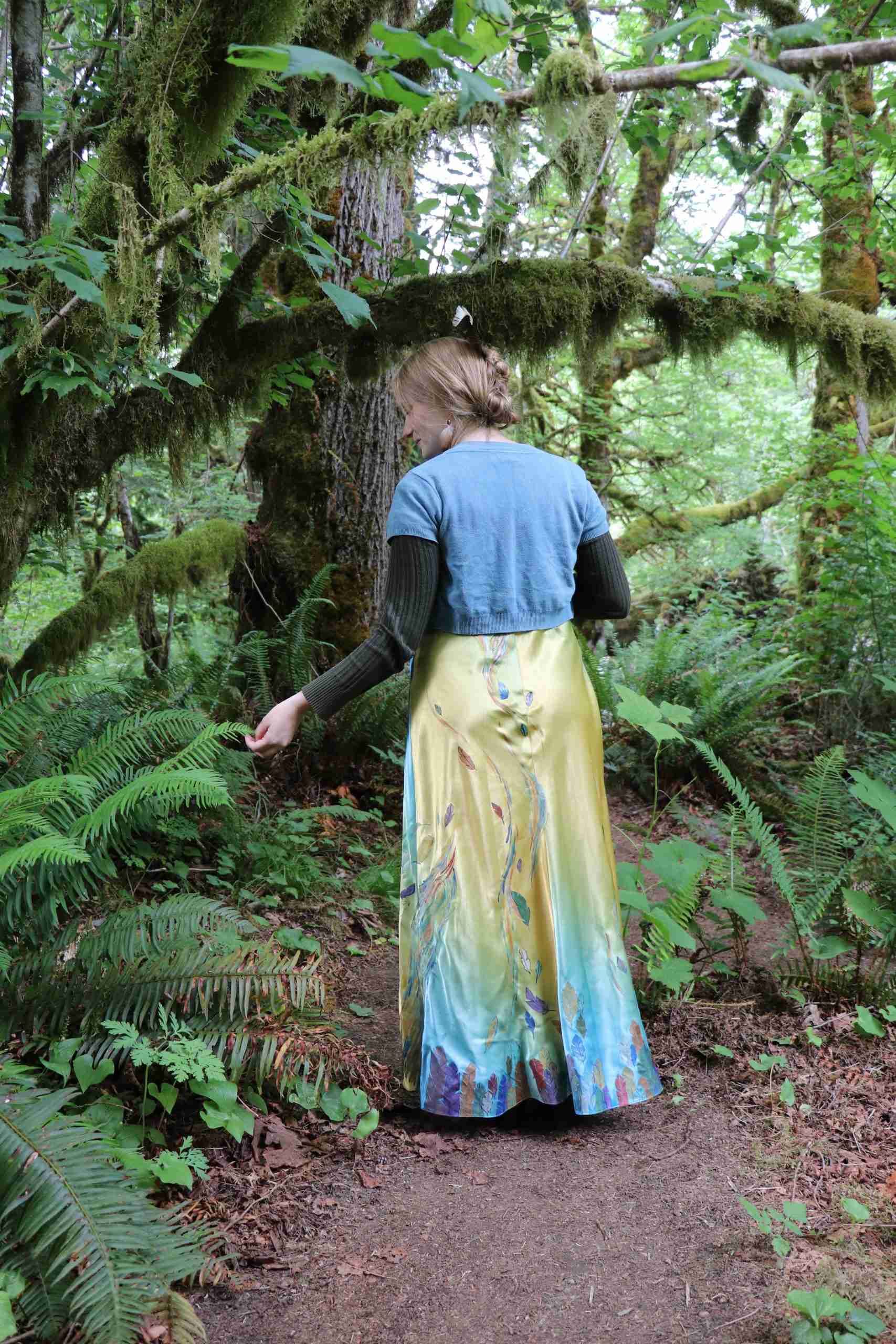 a woman in a dress walking through a forest.