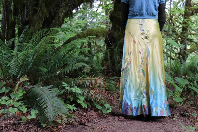 a woman in a long skirt standing in a forest.